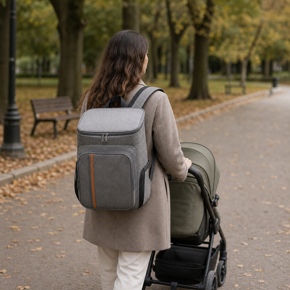Un parent porte un sac à dos à langer gris pendant une promenade avec une poussette