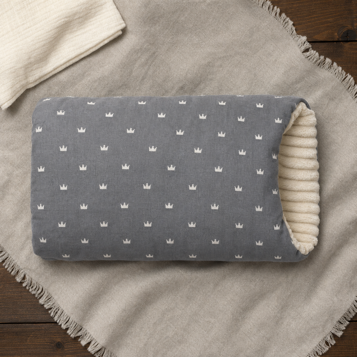 Coussin de bras gris à motifs couronnes, posé à plat sur un tissu clair.