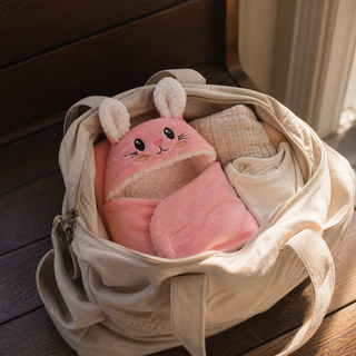 Couverture lapin rose rangée avec des vêtements dans un sac ouvert.